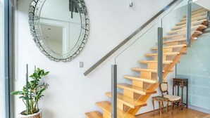 Una escalera moderna con barandillas de vidrio y peldaños de madera, un espejo decorativo y una planta en maceta.