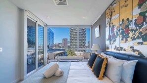 Una habitación de hotel moderna con una cama grande, un balcón con vista a la ciudad y una obra de arte tradicional en la pared.