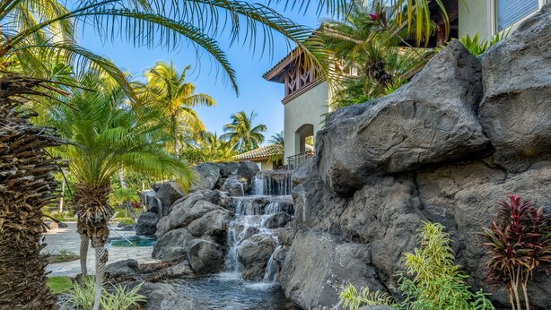 A tropical resort with a waterfall, palm trees, and a pool. - Mauna Lani Fairways #204: Tropical Home w/spa, lanai, lagoon pool & activities (Kamuela)