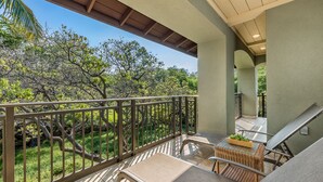 A balcony with two lounge chairs, a small table with a plant, and a view of trees and greenery. - Mauna Lani Fairways #204: Tropical Home w/spa, lanai, lagoon pool & activities (Kamuela)