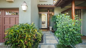 A house entrance with a stone pathway, a wooden porch, and a garage door. - Mauna Lani Fairways #204: Tropical Home w/spa, lanai, lagoon pool & activities (Kamuela)
