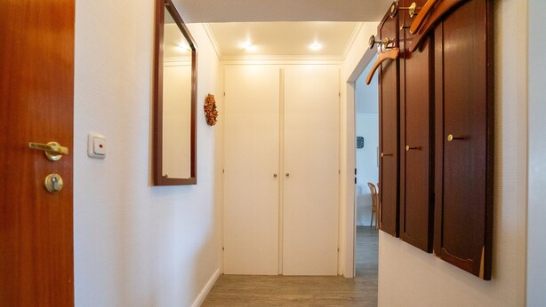 Un pasillo con una puerta de madera a la izquierda, un perchero a la derecha y un par de puertas al fondo.