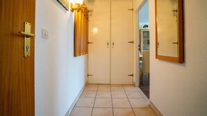 Un pasillo con puerta de madera, un aplique en la pared y un doble acceso con espejo.