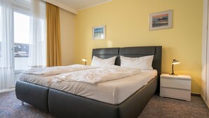 Una habitación de hotel con una cama grande, dos mesitas de noche y un ventanal con cortinas.