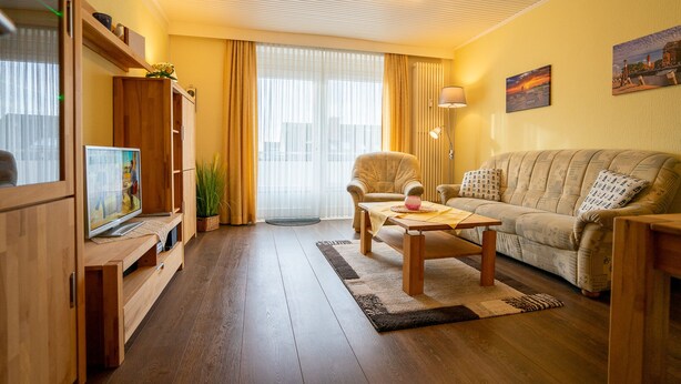 Una sala de estar acogedora con un mueble de madera para entretenimiento, un sofá, una mesa de centro y un ventanal con cortinas.