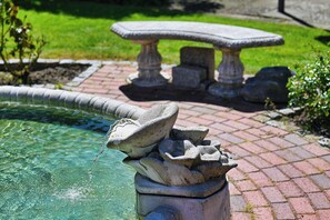 A stone fountain with water spouting from its top, surrounded by a brick pathway and a stone table in a garden setting. - House Klabautermann Apartment 6/1 (Büsum)