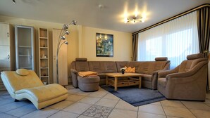 Ein Wohnzimmer mit einer Sofagarnitur, einem Liegesessel, einem Couchtisch und einer Stehlampe.