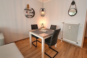 Ein Essbereich mit Tisch, Stühlen, einer Pendelleuchte, einem Wandspiegel und einer Heizung.