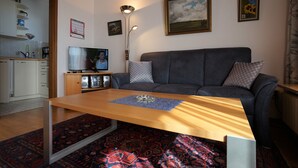 Una sala de estar con sofá, una mesa de centro, un televisor y una cocina al fondo.