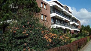 Un edificio residencial de varios pisos con balcones, rodeado de abundante follaje y plantas florecientes.