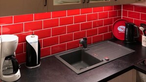 A kitchen with white cabinets, a red tiled backsplash, a coffee maker, a sink, and a red dish rack. - Büsumer Kuschelnest mit Meerblick (Büsum)