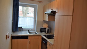 A compact kitchen with wooden cabinets, a microwave, a toaster, and a dishwasher. - Residenz Rosenhof BDH (Büsumer Deichhausen)