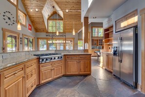 Une cuisine moderne avec des meubles en bois, un réfrigérateur en acier inoxydable et un grand îlot central doté d’une plaque de cuisson intégrée.