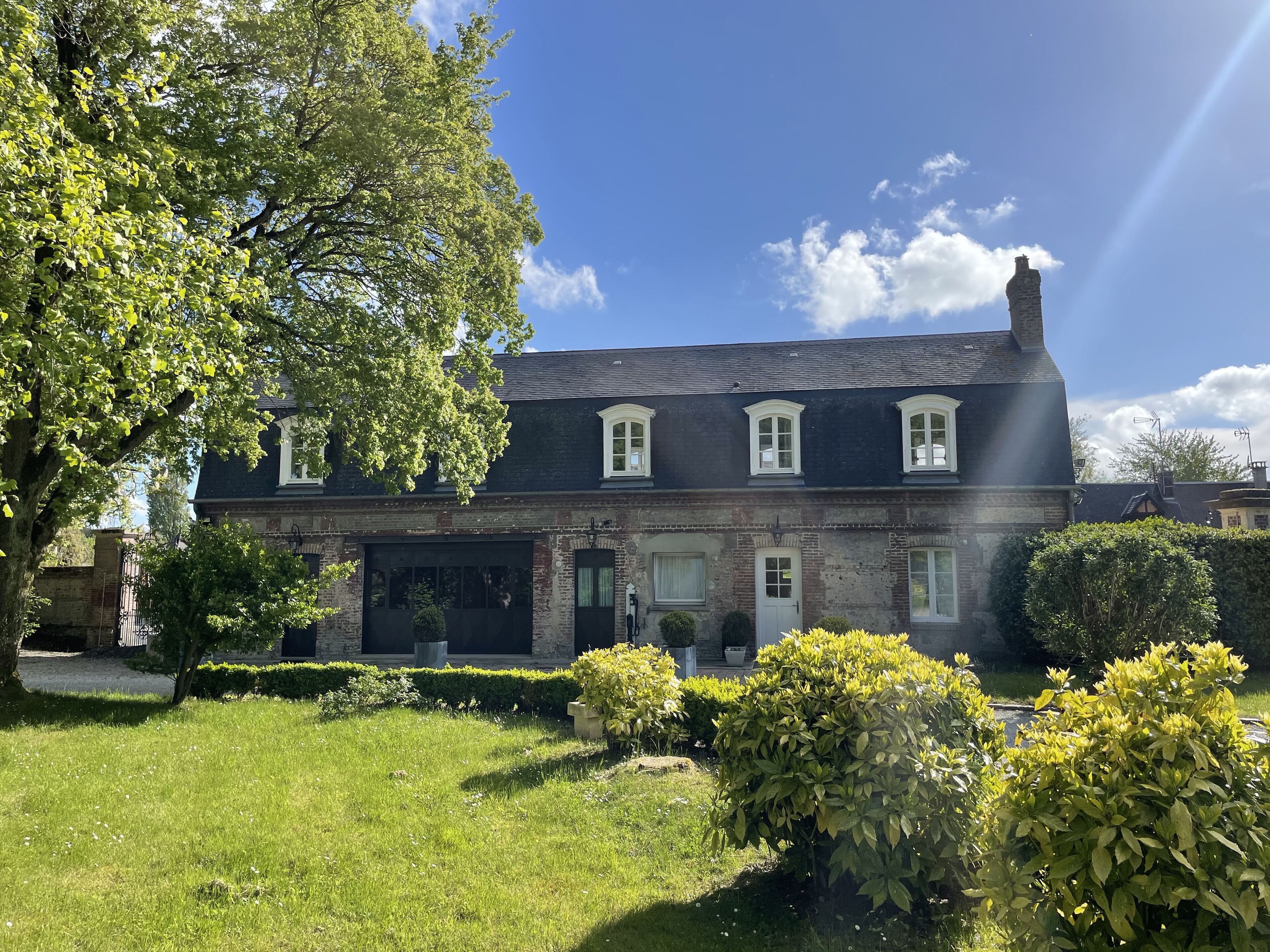 Une maison à deux étages, avec un toit sombre, des encadrements de fenêtres blancs et une façade en briques.