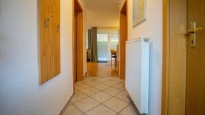 A hallway with wooden doors and a tiled floor leading to a room with a radiator and a chair. - Wohnung Felber am Ostdeich (Büsum)