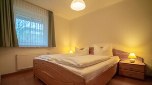 A neatly made bed with white linens, a wooden headboard, and a bedside table with a lamp. - Wohnung Felber am Ostdeich (Büsum)
