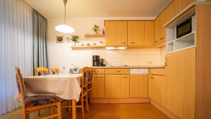 A compact kitchen with wooden cabinets, a dining table with chairs, and a built-in microwave shelf. - Wohnung Felber am Ostdeich (Büsum)