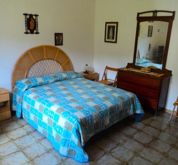 A bedroom with a bed, a wooden dresser, a chair, and a mirror. - Villa Rudolph in Scopello (Sicilia)