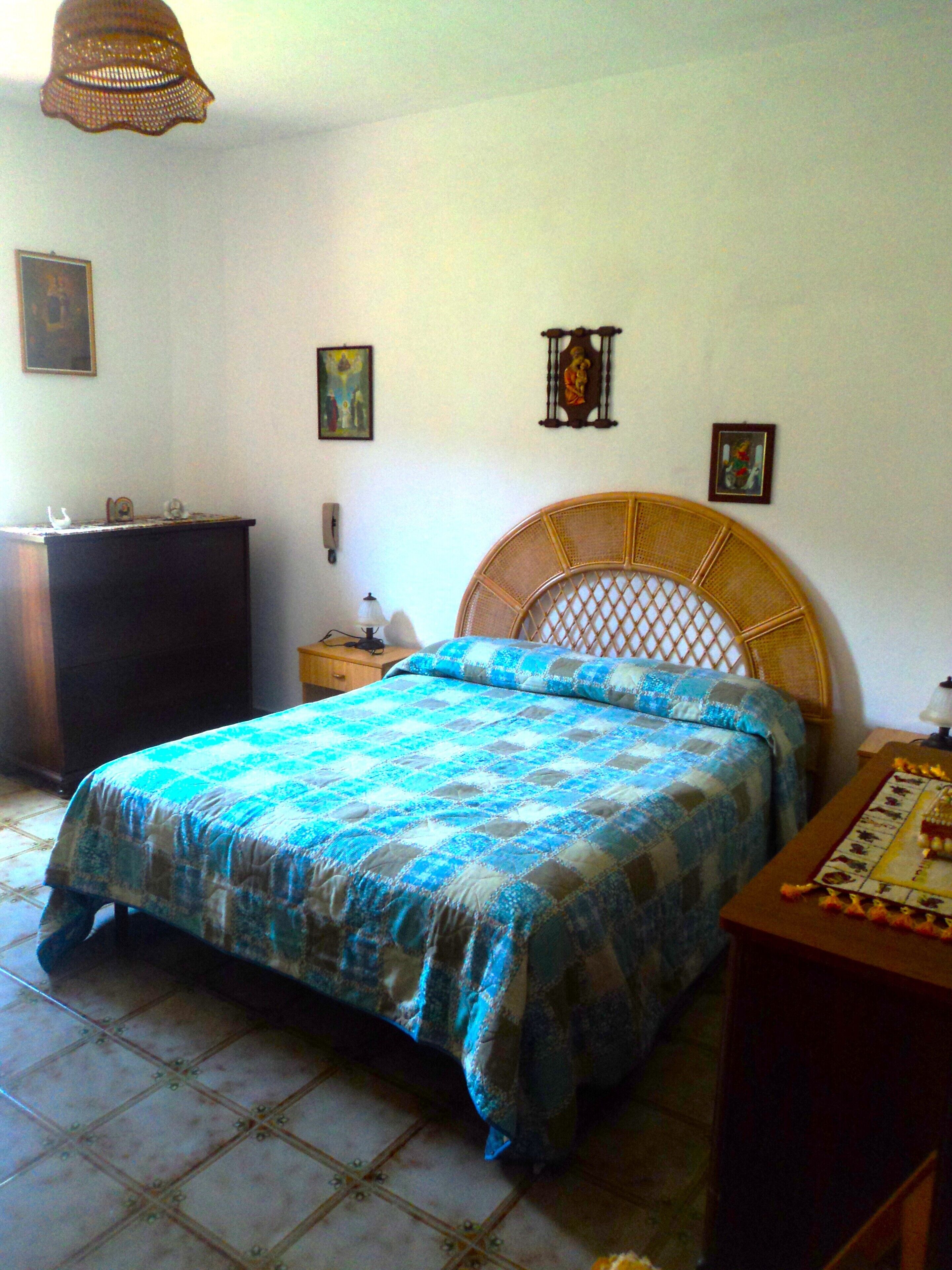 A bedroom with a bed, a dresser, a nightstand, a lamp, and a wall hanging.