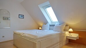 Et soveværelse med skråvæg, ovenlys, seng, sengebord med lampe og et lille billede på væggen.