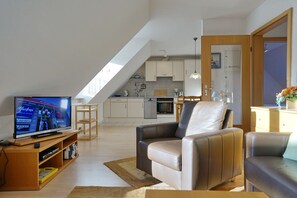 Una sala de estar moderna con televisor, sillones de cuero y una cocina al fondo.