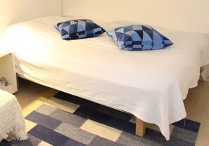 A bed with a white sheet and two blue patterned pillows, a checkered rug, and a white bedside table with a lamp. - Southern Stockholm Center Large Room (Stockholm)