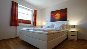Een slaapkamer met een bed, een nachtkastje, een lamp, een raam met gordijnen en een schilderij aan de muur.