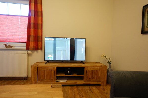 Una sala de estar con un mueble de madera para entretenimiento, un televisor, un radiador y una ventana con cortinas.
