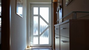 A hallway with a large glass door leading to a bright room, tiled floor, and a modern kitchen area with cabinets and a countertop. - Haus Meereskönig Wohnung 2 (Büsum)