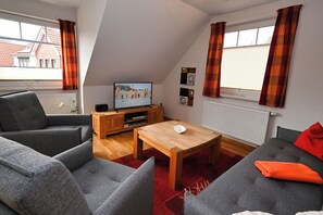 Ein modernes Wohnzimmer mit Fernseher, grauen Sofas, einem Holztisch und einem roten Teppich.