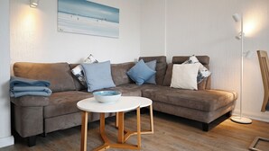 Ein modernes Wohnzimmer mit einem braunen Ecksofa, einem weißen runden Tisch auf Holzbeinen und einer Stehlampe.