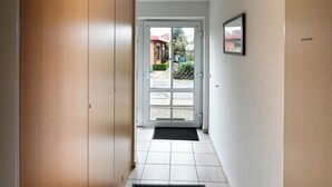 A hallway leading to a door with a view of a garden and a building outside. - Haus Schäfer Wohnung 1 in Ruhiger Lage (Büsum)