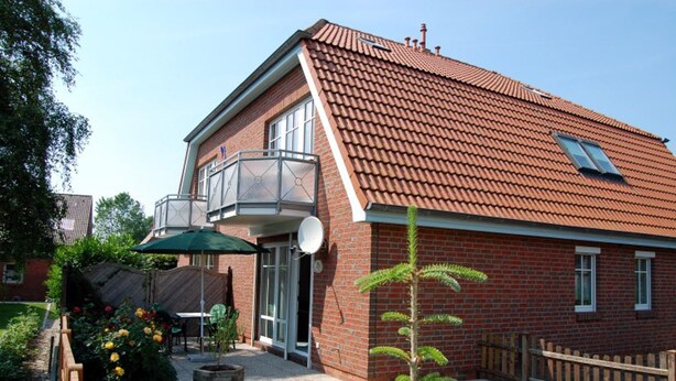 A two-story brick house with a red-tiled roof, a balcony, and a satellite dish. - Haus Schäfer Wohnung 1 in Ruhiger Lage (Büsum)