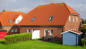 Een herenhuis met twee verdiepingen, een rode dakbedekking, een klein tuinhuisje en een verzorgd gazon.