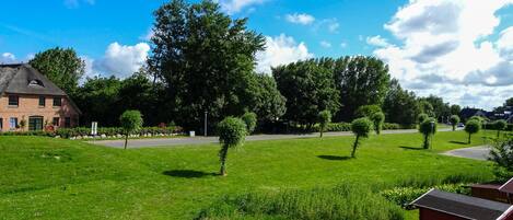 A grassy area with a brick building, trees, and a clear sky.