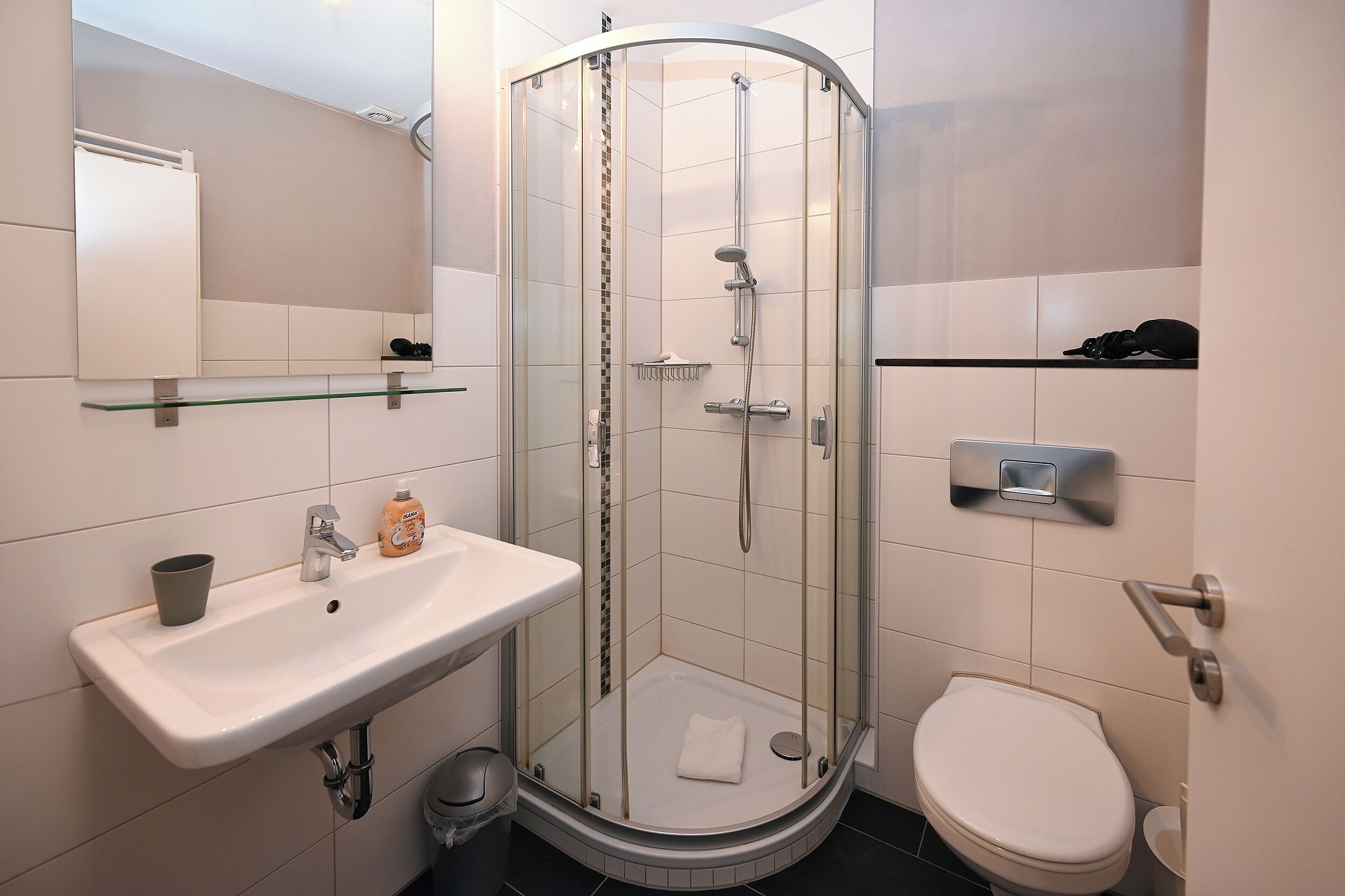 Un bagno moderno con doccia vetro, lavandino con specchio e water.