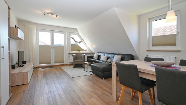 Ein modernes Wohnzimmer mit Essbereich, einer Couch, einem Fernseher und einem Fenster mit Jalousien.