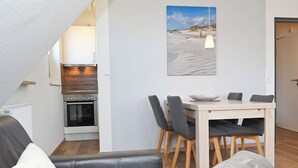 Ein modernes Wohnzimmer mit einer Couch, einem Esstisch mit Stühlen, einer Küchenzeile mit einem Backofen und einem Gemälde an der Wand.