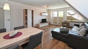 Ein moderner Wohnraum mit Essbereich, einer Couch, einem Fernseher und einem Bücherregal.