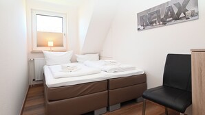 Ein Schlafzimmer mit einem Bett, einem Sessel, einem Heizkörper, einem Fenster und einem Wandbild.