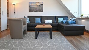 En moderne stue med en modulsofa, en lænestol, et lille bord og et gulvtæppe med geometriske mønstre.
