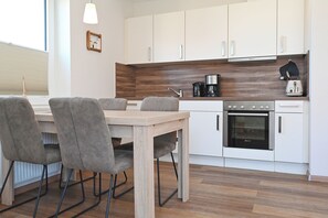 Une cuisine moderne avec des armoires blanches, un plan de travail en bois, un four encastré et un coin repas comprenant une table en bois et des chaises grises.