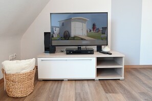 A television on a wooden stand with a remote, a white cabinet below, and a wicker basket with a pillow.
