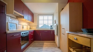A compact kitchen with red cabinets, a built-in oven, and a window providing natural light.