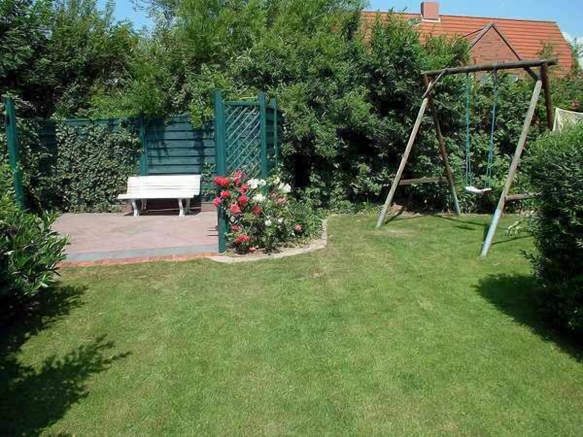 Ein gepflegter Garten mit einer Bank, einer Schaukel und einem grünen Tor.