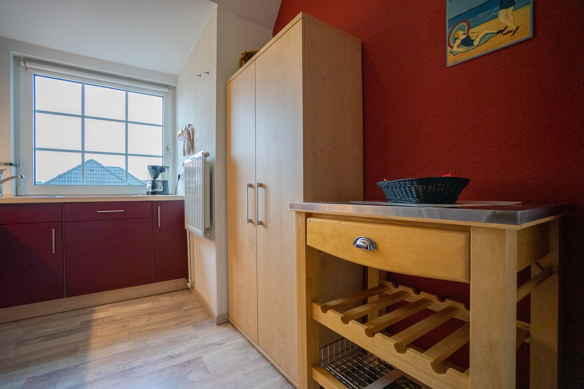 Een keuken met houten kasten, een wijnrek en een raam met uitzicht op een gebouw.