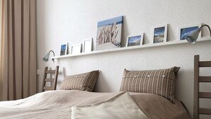 Een netjes opgemaakt bed met een gewatteerde deken, een nachtkastje en een wandplank met ingelijste foto's.