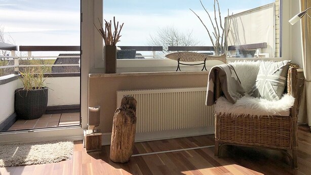 Een balkon met een rieten stoel, een plant in pot en een rustieke houten sculptuur.