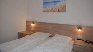 Una camera da letto con una testiera in legno, due comodini con lampade, un letto con lenzuola bianche e un quadro raffigurante una spiaggia.