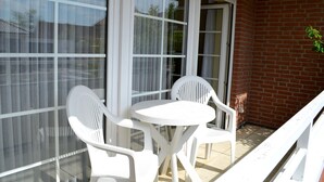 Un balcone con una porta in vetro, sedie in plastica bianca e un tavolino rotondo.